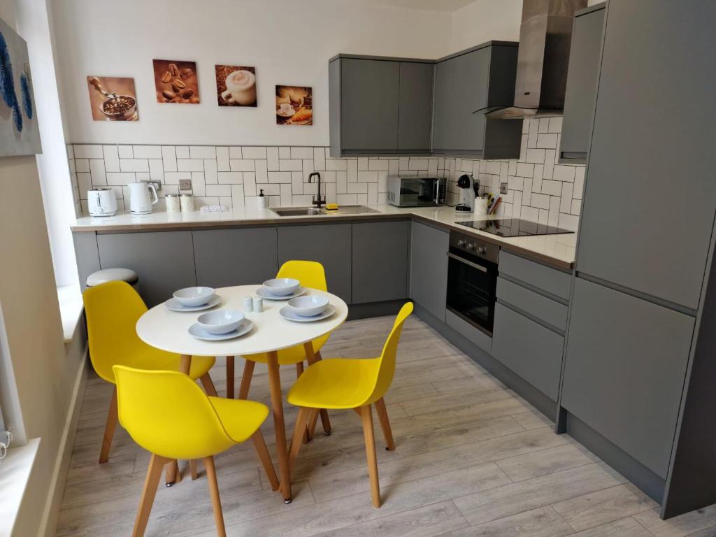 a kitchen with a table and yellow chairs at Suffolk House Apartments HU1 in Hull