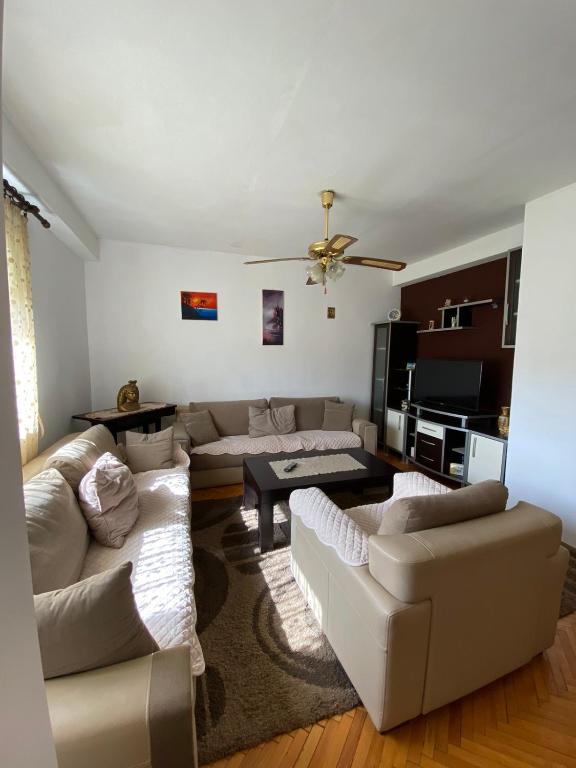 a living room with white furniture and a ceiling fan at Dena Apartment in Kumanovo