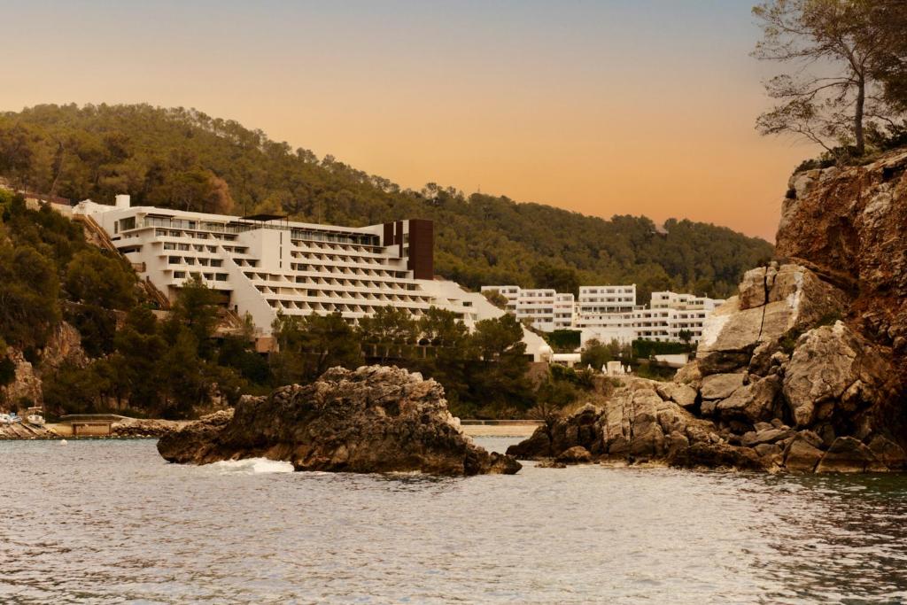 duży biały budynek na wzgórzu obok wody w obiekcie Cala San Miguel Hotel Ibiza, Curio Collection by Hilton, Adults only w mieście Puerto de San Miguel