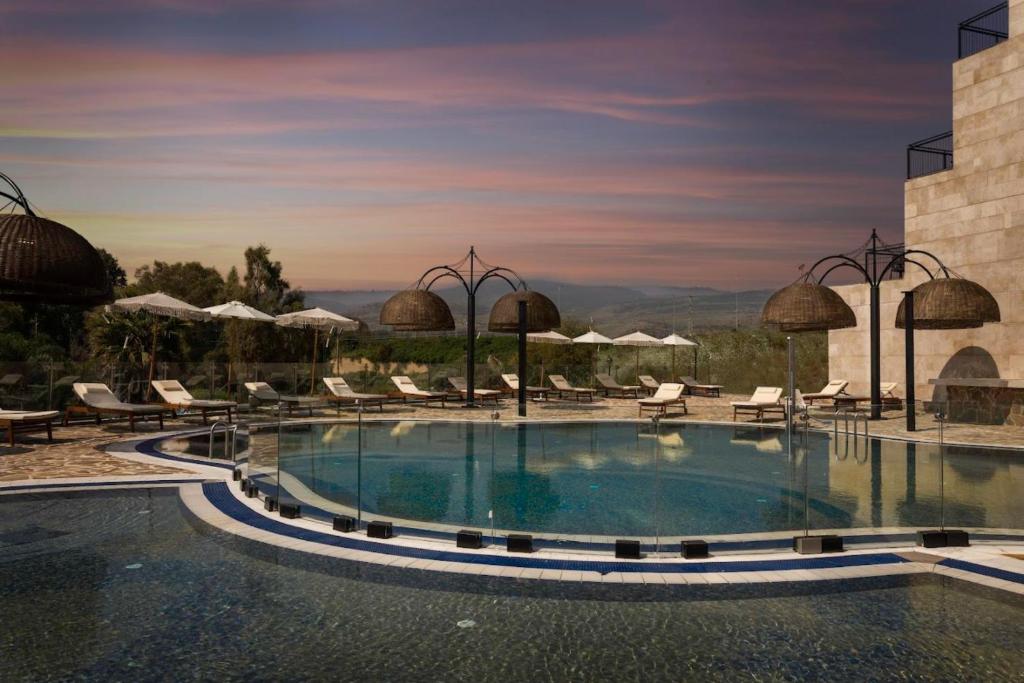 una piscina en un complejo con sillas y sombrillas en Yarden Estate Boutique Hotel en Yesod Hamaala