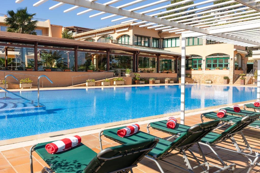 Hotel Sa Punta - Adults Only في بيغور: مسبح وكراسي خضراء ومبنى