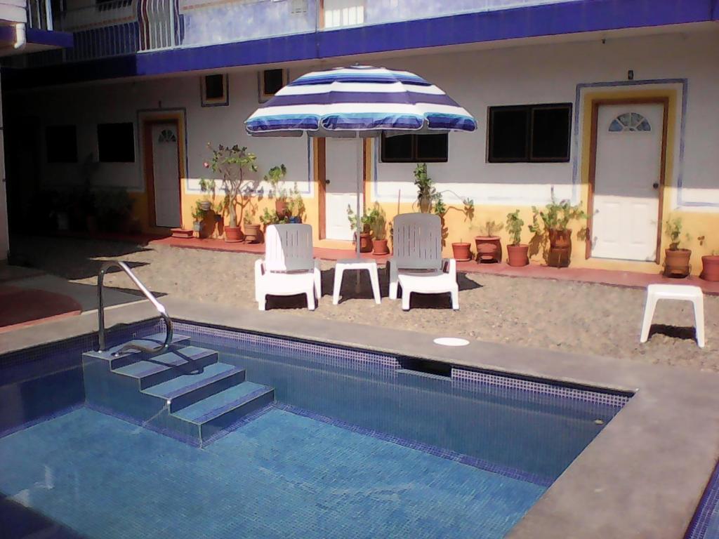 a swimming pool with two chairs and an umbrella at Hotel Sarabi in Barra de Navidad