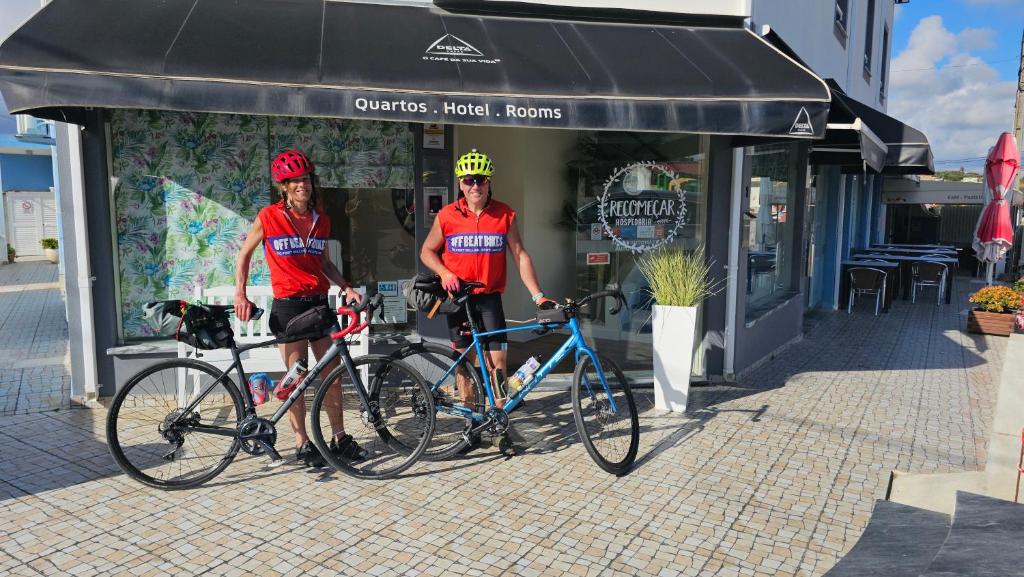 deux hommes sont debout avec leurs vélos devant un magasin dans l'établissement Sea & Sun Hospedaria Recomeçar, à Torres Vedras