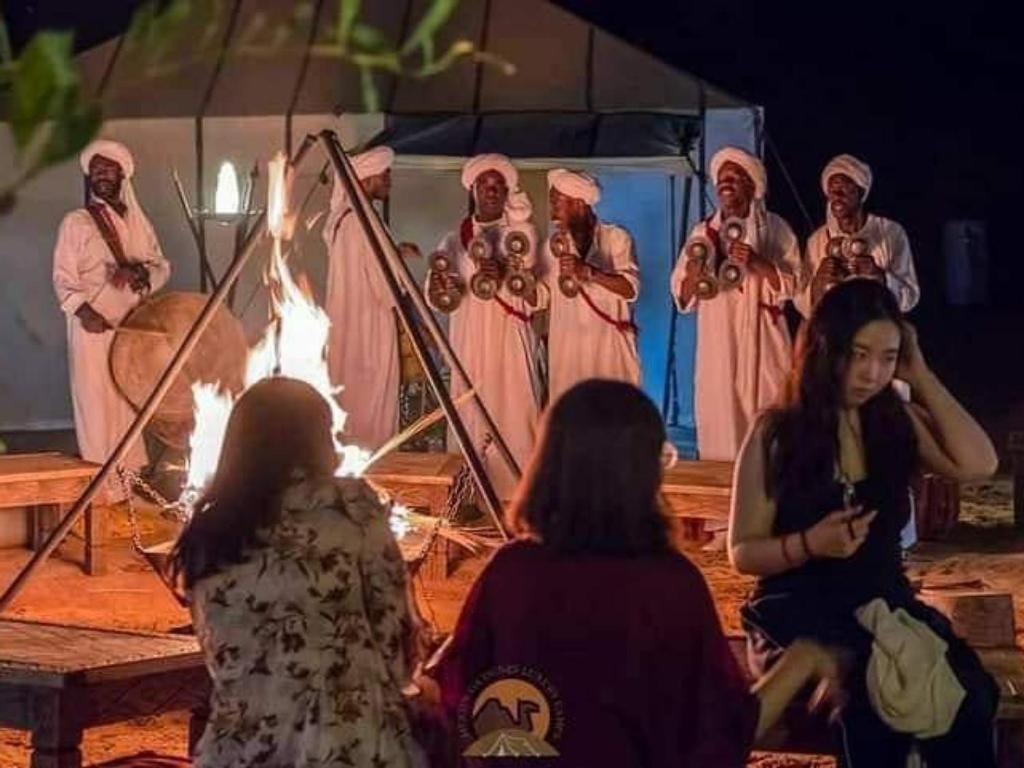 eine Gruppe von Menschen, die um ein Feuer stehen in der Unterkunft Services Luxury Camp in Merzouga