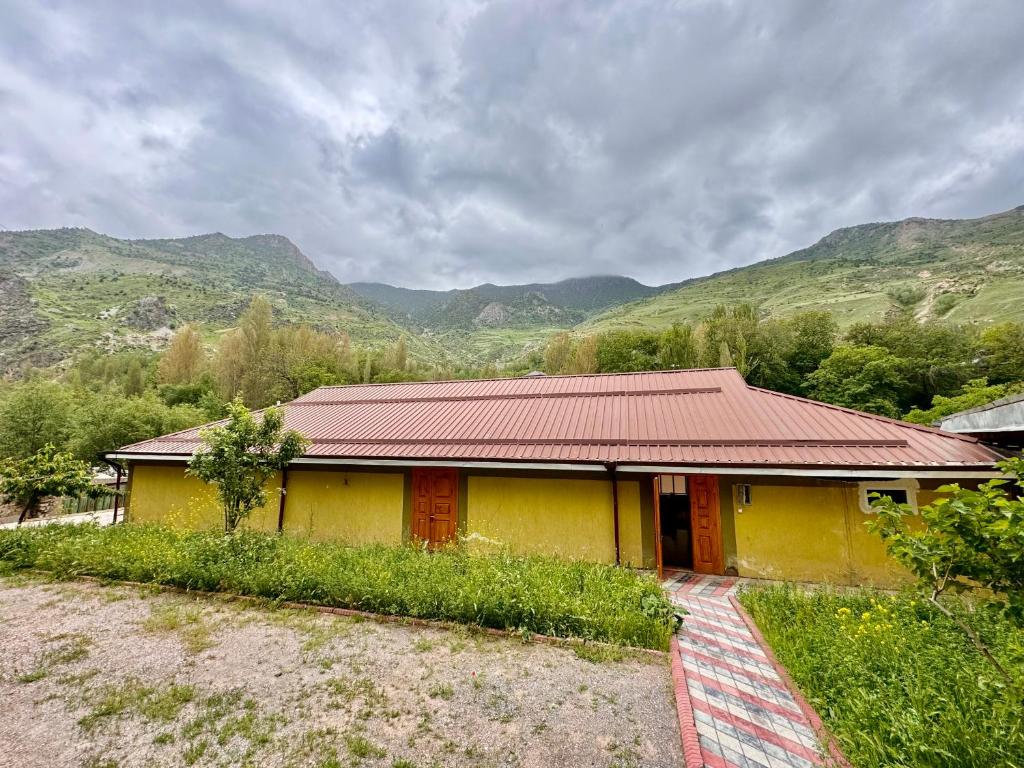 a yellow house with a red roof with mountains in the background at Panjrud guest house in Panjakent