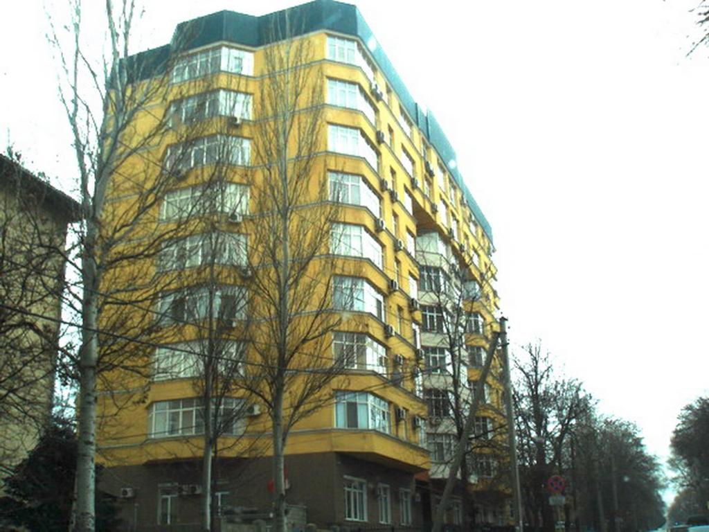 a tall yellow building with a tree in front of it at Bishkek Residence Apartment in Bishkek