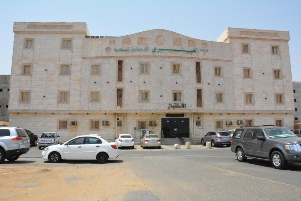 ein großes Steingebäude mit Autos auf einem Parkplatz in der Unterkunft العيرى للشقق المخدومه جازان 1 in Dschāzān