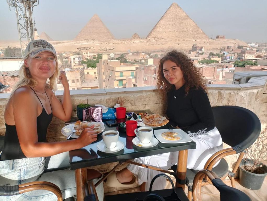 two women sitting at a table with food in front of the pyramids at Pyramids station View in Cairo