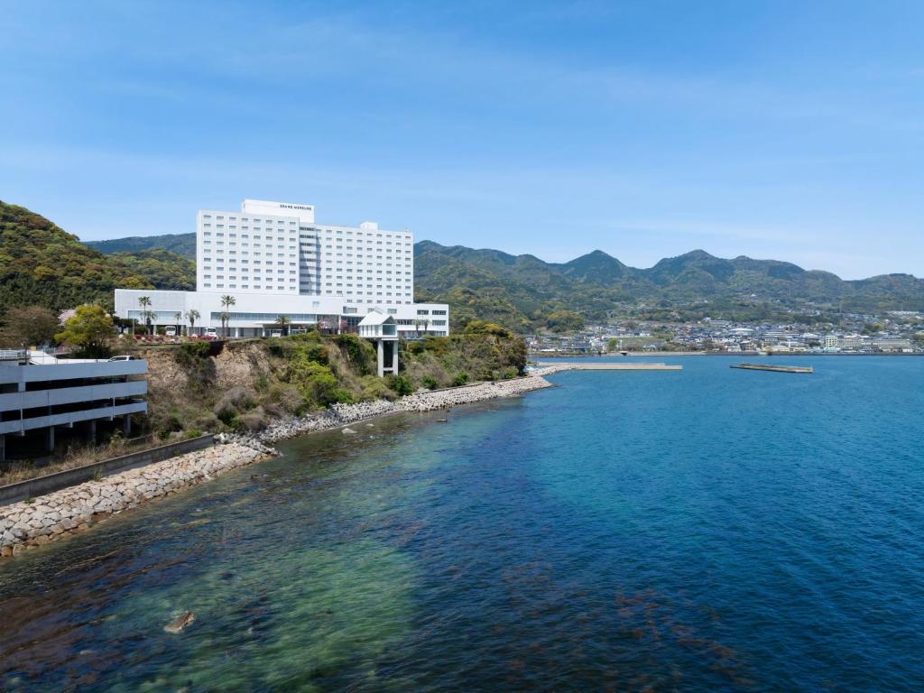 Grand Mercure Beppu Bay Resort & Spa في بيبو: مبنى كبير على جانب تجمع المياه