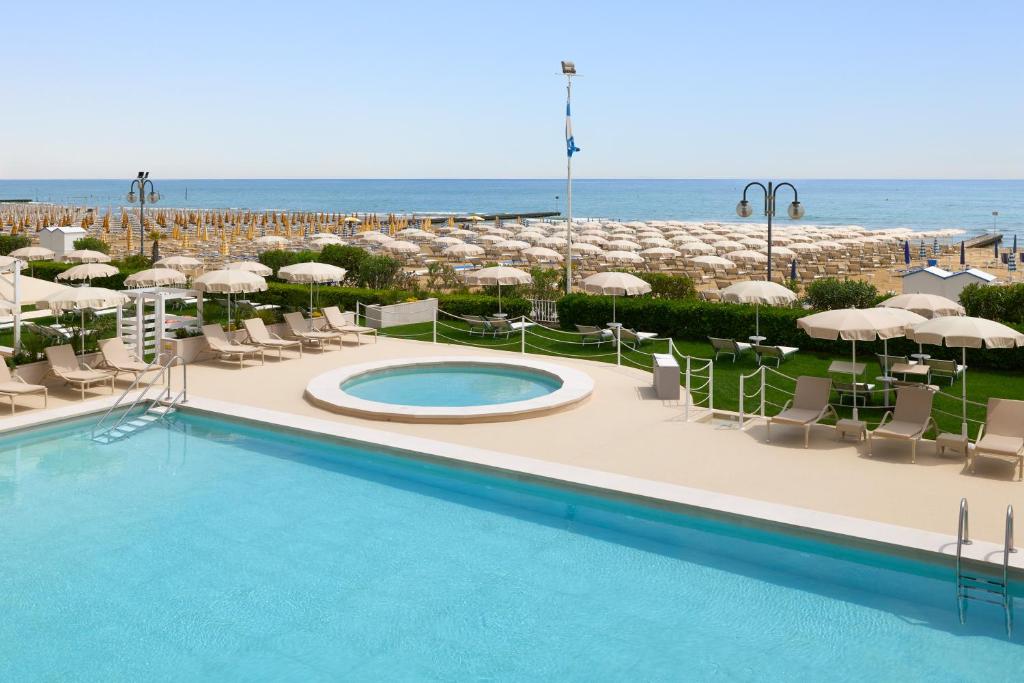 a pool with chairs and umbrellas and the ocean at Hotel Aurora in Lido di Jesolo