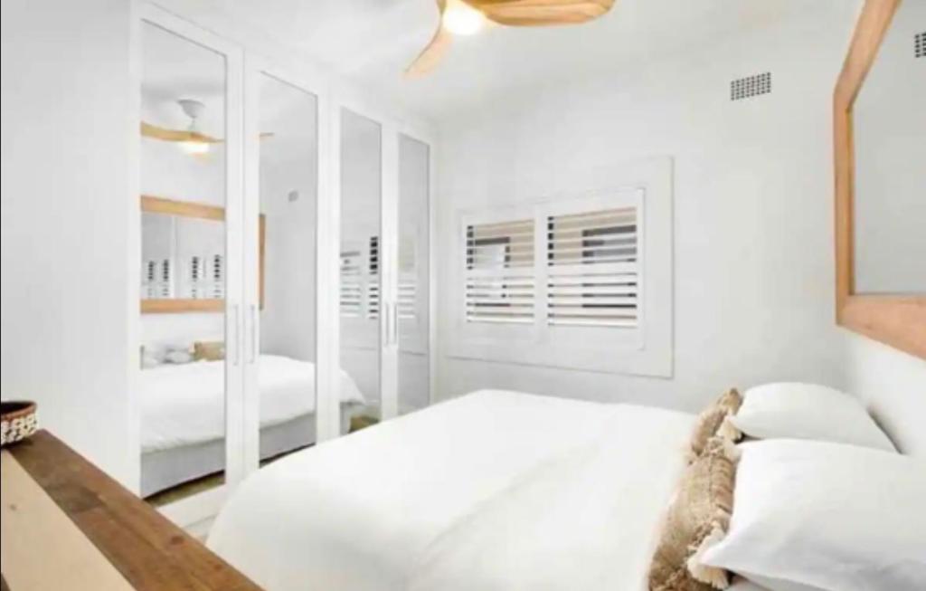 a white bedroom with a bed and a mirror at Bondi Bliss ~ Stylish & Comfy Gem ~ Walk to Beach! in Sydney