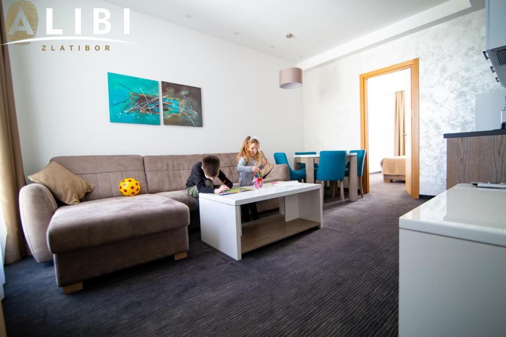 uma sala de estar com um sofá e uma criança sentada numa mesa em Alibi Zlatibor Inn em Zlatibor