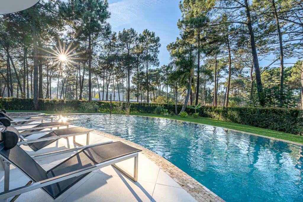 uma piscina com espreguiçadeiras e árvores em Moradia T5 com golfe e piscina na Caparica em Aroeira