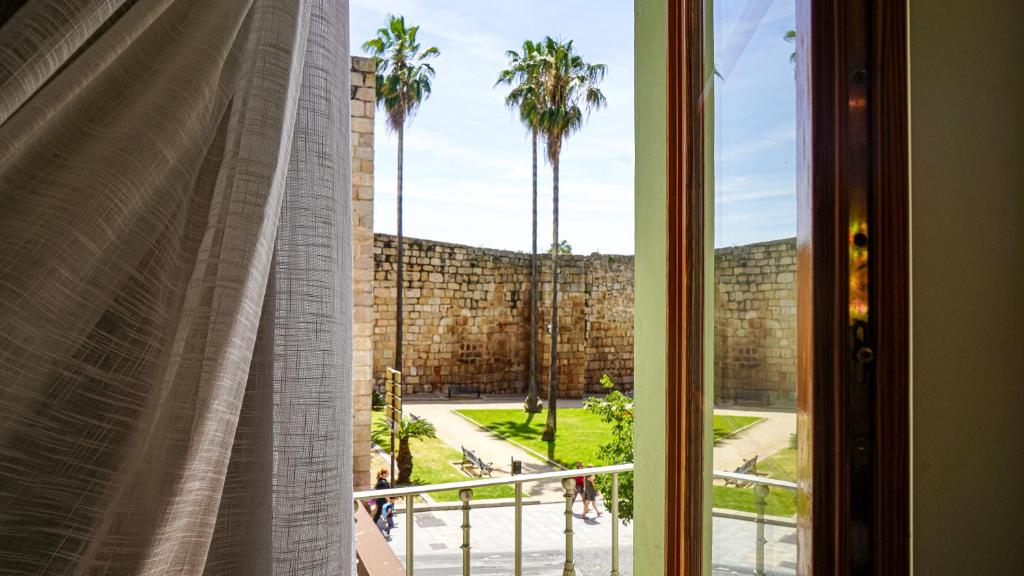 ventana con vistas a la pared y a las palmeras en Apartamentos Puente Romano Suites Parking Gratis, en Mérida