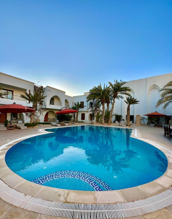 a large blue pool in a courtyard with palm trees at Palm Djerba Suites in Mezraya