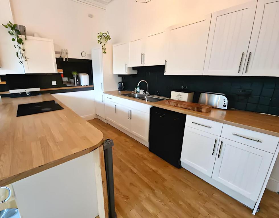 a kitchen with white cabinets and a wooden floor at Central Large 2 Bed, 2 Bath Apt, Parking, Huge Garden, SKY TV, Wifi, Direct Booking Option in Exeter