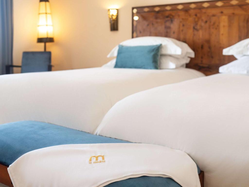 two beds with white sheets and blue pillows in a room at Le Médina Essaouira Thalassa Sea & Spa - MGallery Collection in Essaouira