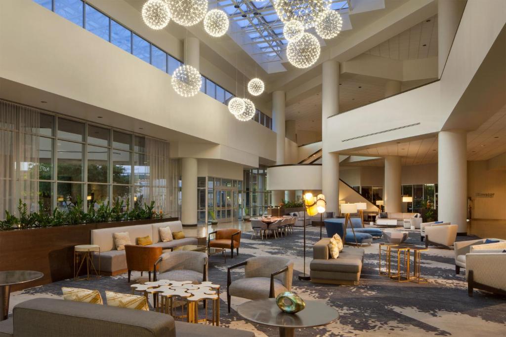 un vestíbulo con mesas, sillas y lámparas de araña en Sheraton Arlington Hotel en Arlington