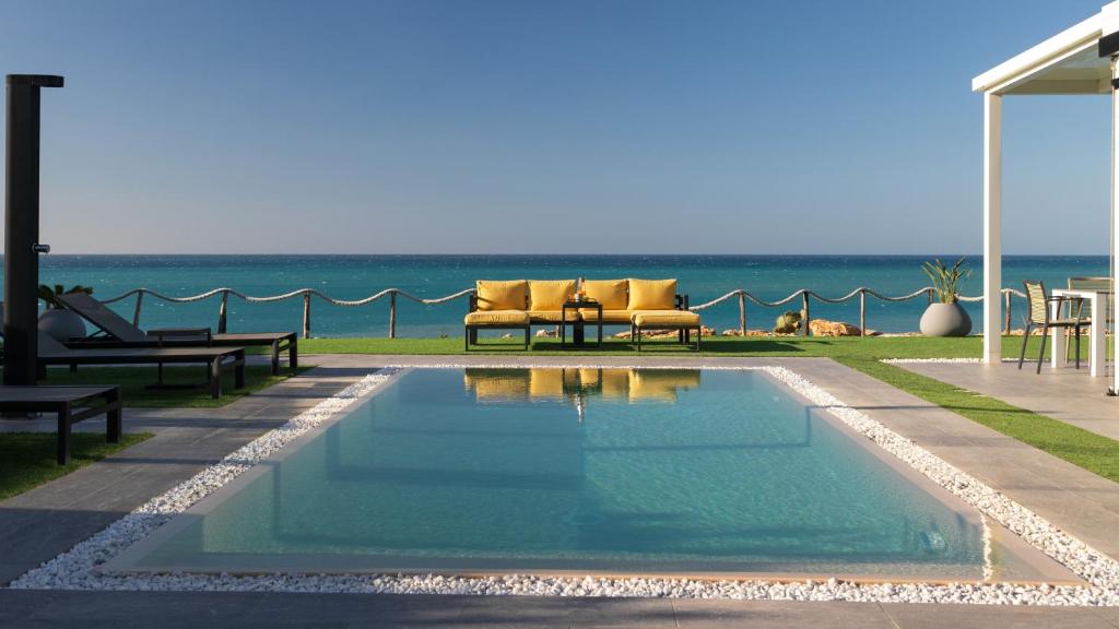 una piscina con sillas y el océano en el fondo en VILLA SABBIE ROSSE 6, Emma Villas en Ovile la Marinella