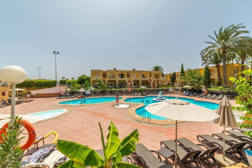 a resort pool with chairs and an umbrella at Sol y mar maspalomas in Maspalomas