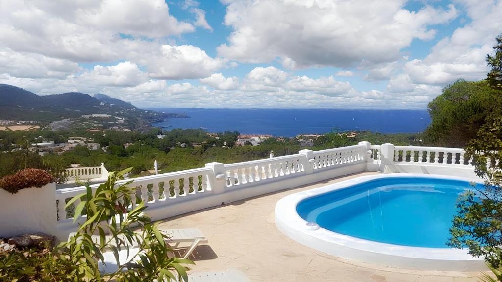 a swimming pool with a white fence and the ocean at 5 bedrooms villa at Sant Josep de sa Talaia 900 m away from the beach with sea view private pool and enclosed garden in Sant Josep de Sa Talaia