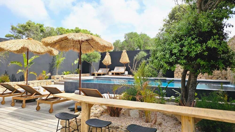 un patio avec des chaises et des parasols ainsi qu'une piscine dans l'établissement Hôtel Les Suites Du Maquis, à Bonifacio