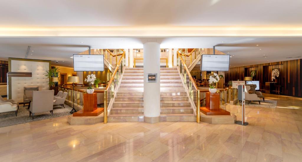 a lobby with a staircase with chairs and tables at Mövenpick Hotel & Casino Geneva in Geneva