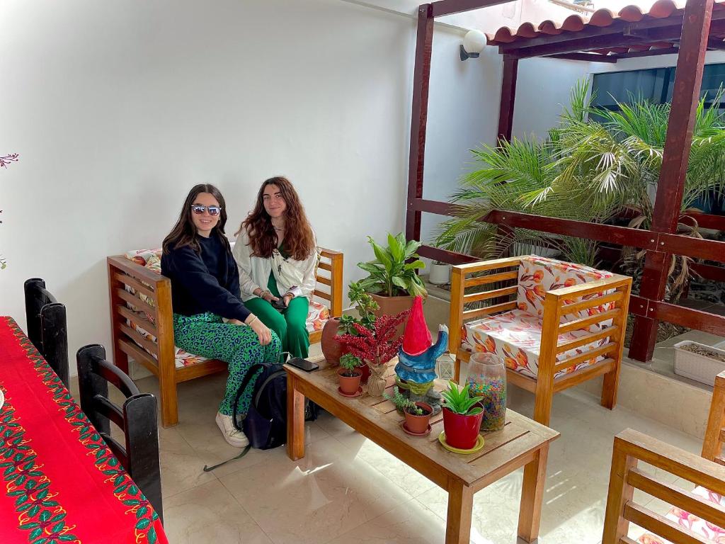 萬查科的住宿－HUANCHACO GARDENS，两个女人坐在椅子上,在一间种有盆栽植物的房间