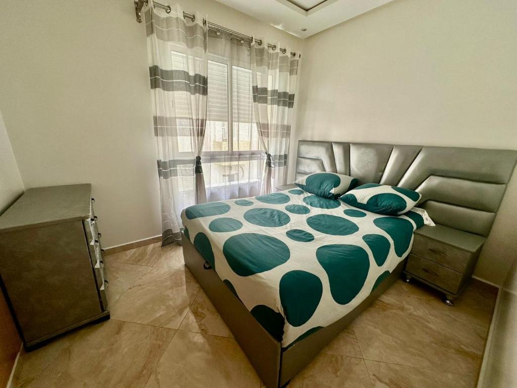 superbe appartement en résidence balnéaire في بوزنيقة: غرفة نوم مع سرير لحاف أخضر و أبيض