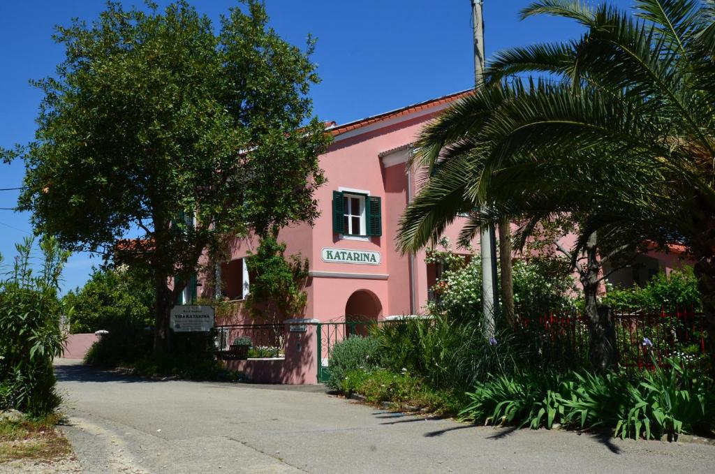 un bâtiment rose avec un palmier devant lui dans l'établissement Villa Katarina Mali Lošinj, à Mali Lošinj
