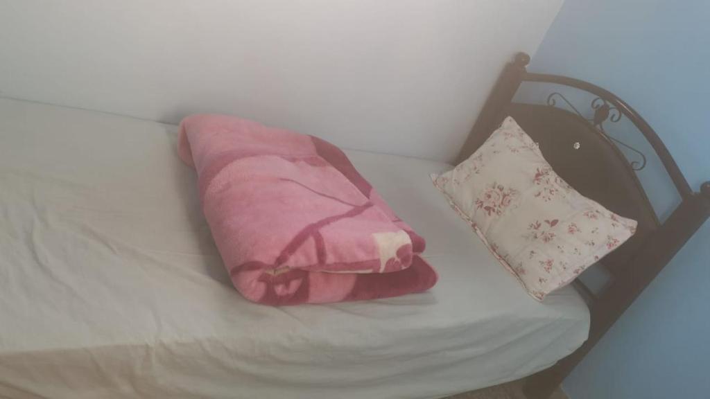 Una manta rosa y una almohada sobre una cama. en Chambre simple, en Agadir