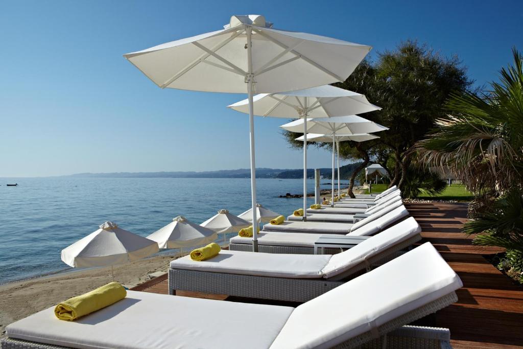 a row of white chairs and umbrellas on a beach at Afitis Boutique Hotel in Afitos