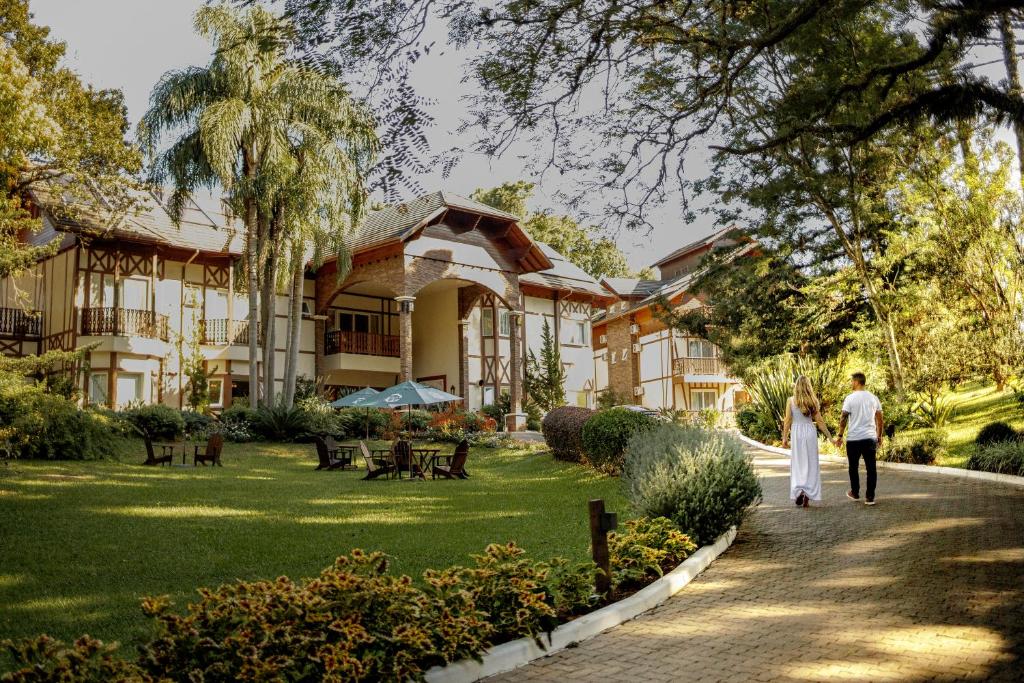 a man and a woman walking down a path in front of a building at Hotel Jardins da Colina in Nova Petrópolis