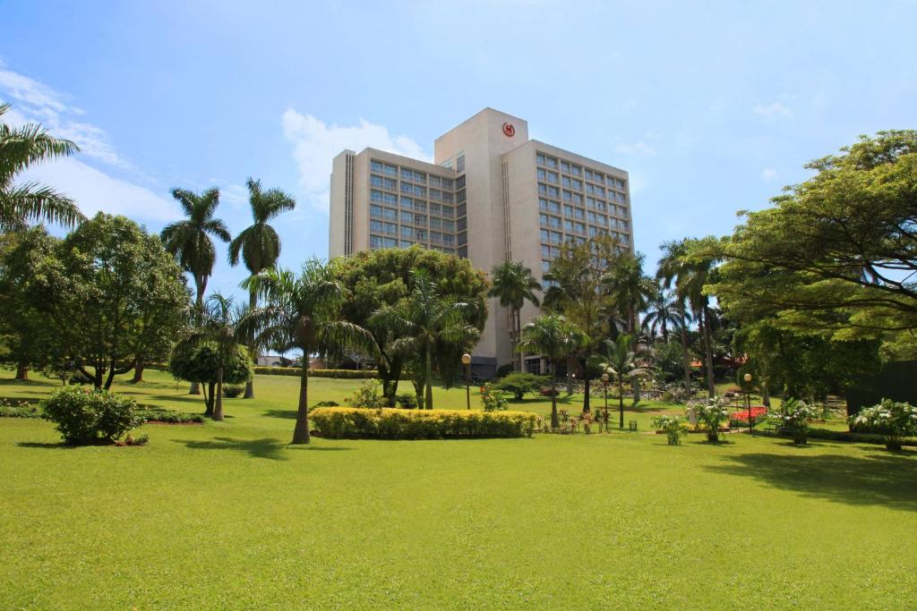 Sheraton Kampala Hotel في كامبالا: مبنى كبير في حديقة بها أشجار وعشب