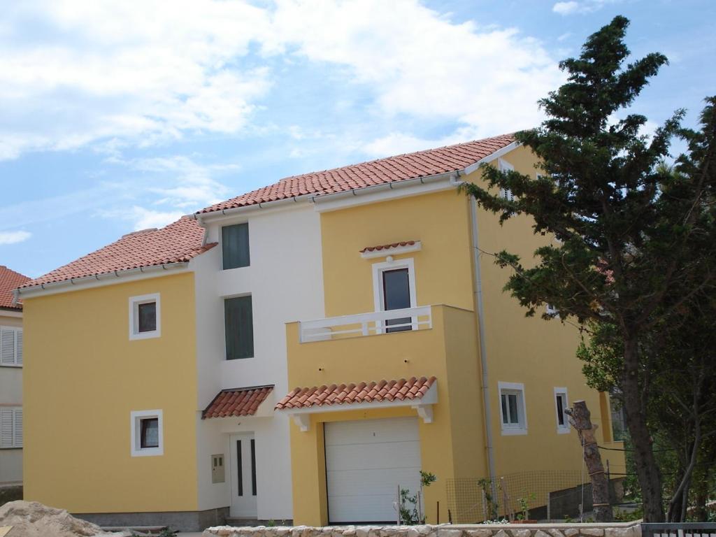 een geel en wit huis met een garage bij Apartments Ivanov in Novalja