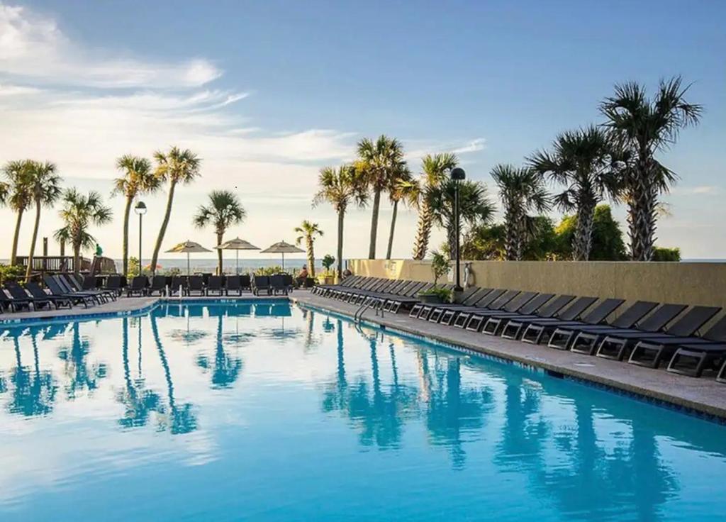 a large swimming pool with chairs and palm trees at Oceanfront Paradise/Waterpark/pools/lazyriver in Myrtle Beach