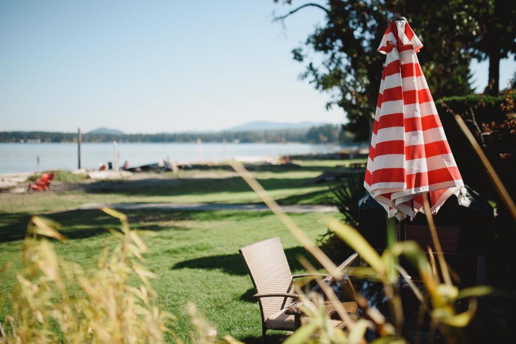 einen Regenschirm und einen Stuhl im Gras in der Nähe des Wassers in der Unterkunft Beach Acres Resort in Parksville