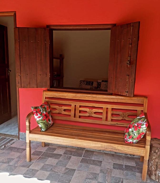 a wooden bench against a red wall with a mirror at Villa Pareto Guest House in Macaé