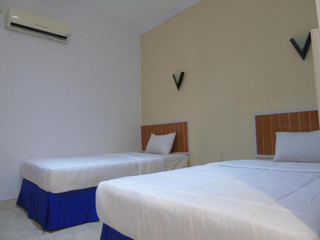 Dos camas en una habitación con sábanas blancas. en Hotel Permata Zamrud, en Cirebon
