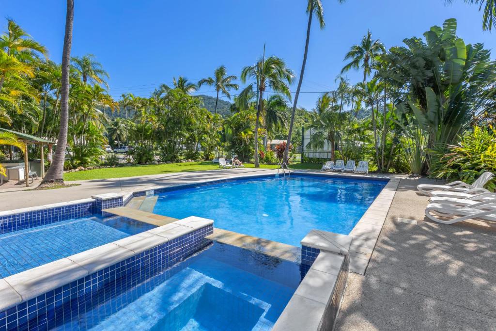 a swimming pool with chairs and palm trees at Tasman Holiday Parks - Airlie Beach in Airlie Beach