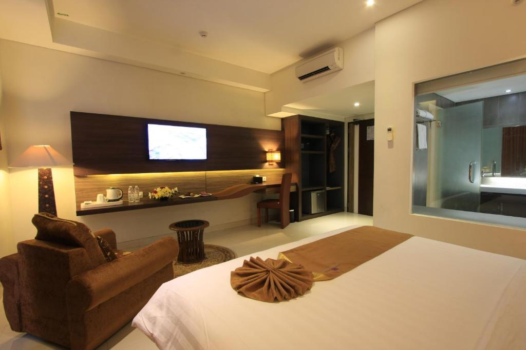 a bedroom with a bed and a chair and a television at Crystal Lotus Hotel Yogyakarta in Yogyakarta