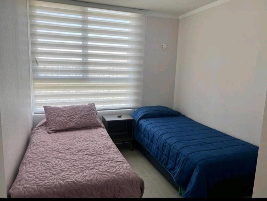Un dormitorio pequeño con dos camas y una ventana. en Departamento a pasos de Enjoy, en Coquimbo