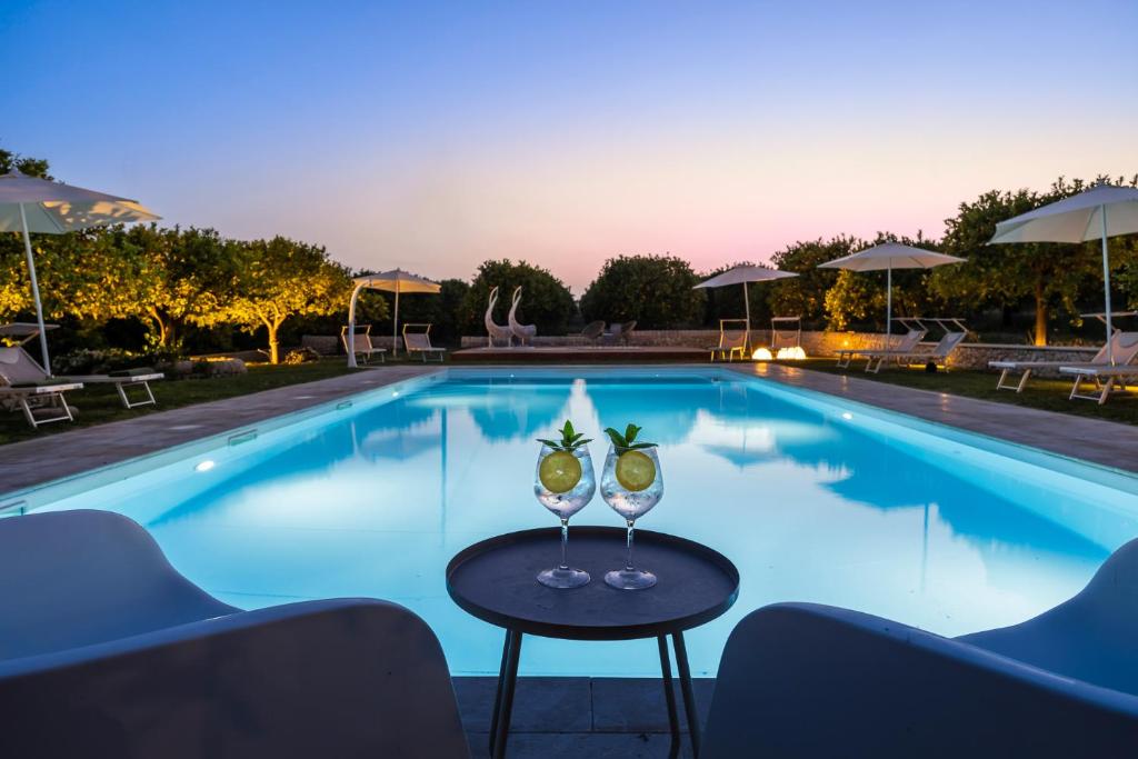a pool with two glasses on a table in front of it at Fiore di Vendicari B&B - Sicilian Charme, Lemon Grove and Sea in Noto