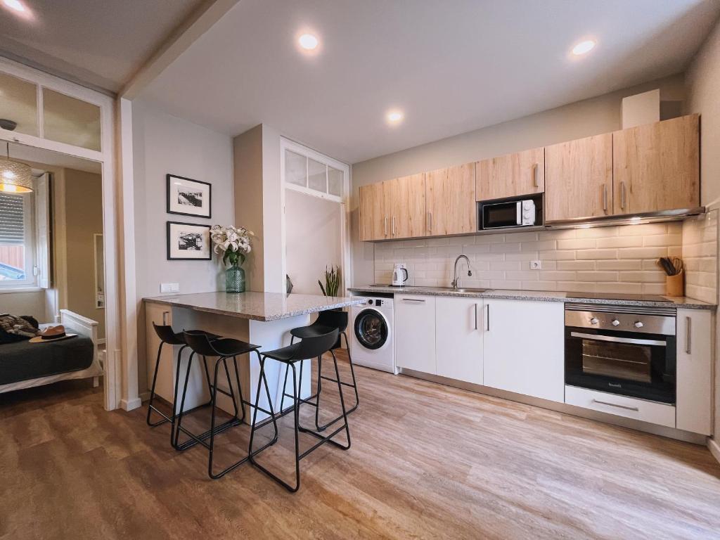 a kitchen with white cabinets and a island with bar stools at Casinha Amarela in Figueira da Foz