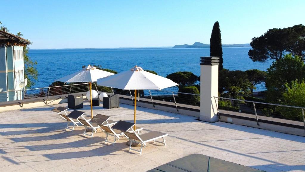 GARDA BLUE HOME on the lake - pool, solarium and garage في توسكولانو ماديرنو: مظلتين وكراسي على فناء مع المحيط
