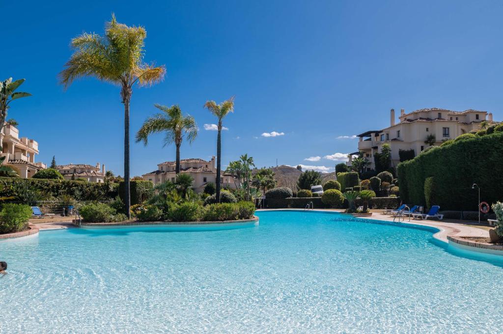 a large swimming pool with palm trees and buildings at 2-bed apartment in Capanes del Golf in Benahavís
