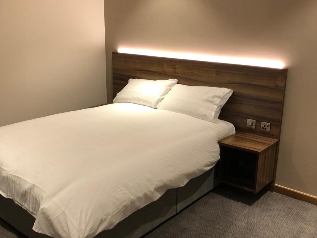 a bedroom with a white bed with a wooden headboard at Rivington Lodge in Bolton