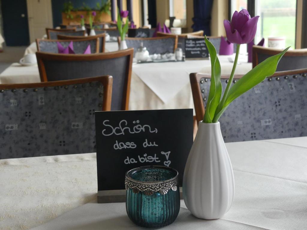 a white vase with a purple flower on a table at Landgasthaus Fecht in Aurich