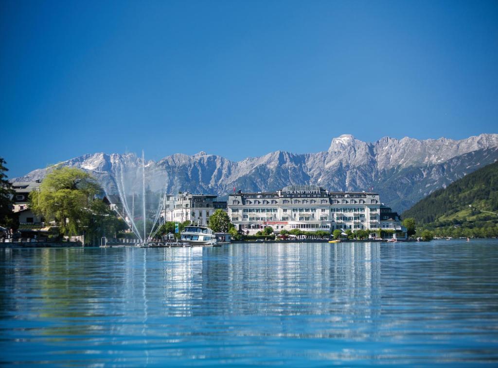 a building on the water with mountains in the background at Grand Hotel Zell am See in Zell am See
