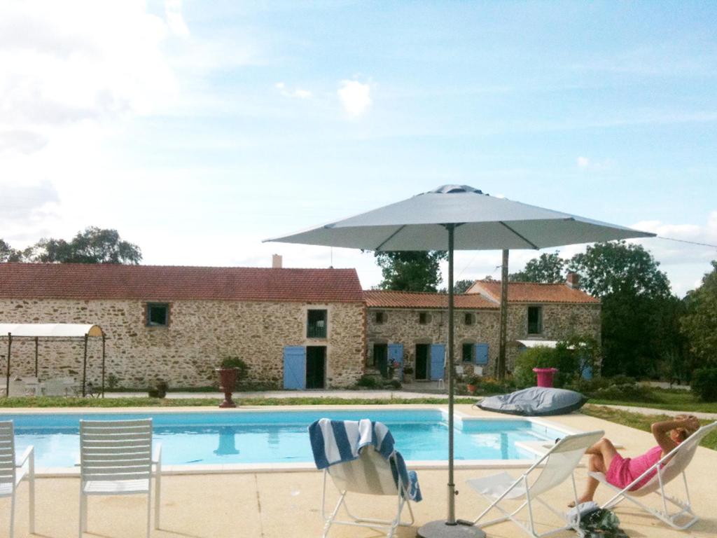 ein Kind, das auf einem Stuhl unter einem Sonnenschirm neben einem Pool sitzt in der Unterkunft Le Clos du Gâts Gîte de charme en Vendée à 15 mn du Parc du Puy duFou in La Gaubretière